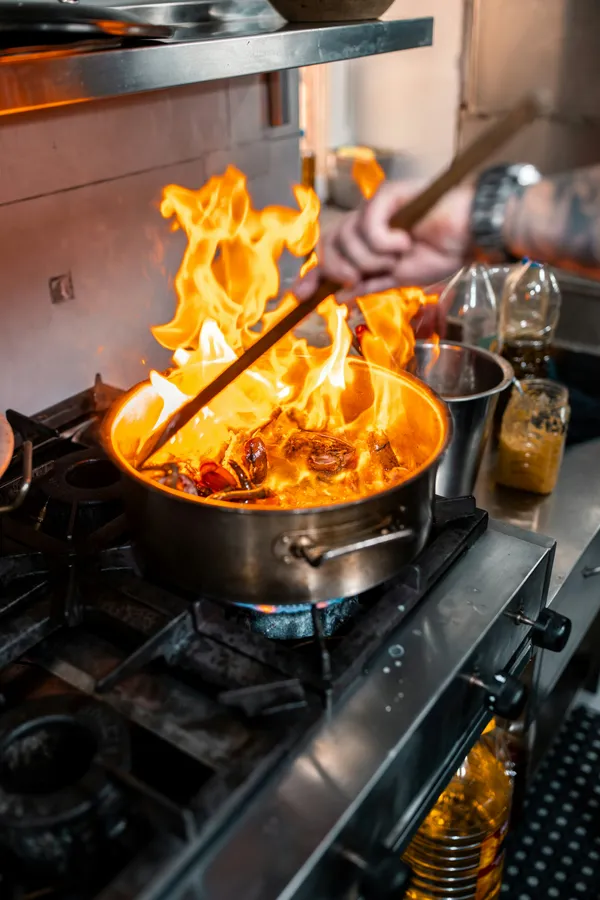 Main d'un cuisinier remuant une poêle en flammes